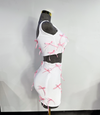 A two-piece skirt set with a white fitted tank top and a white high-waisted mini skirt, both adorned with pink ribbon bows and rhinestone accents by Bellz Couture in Detroit. shown on mannequin against a plain wall.
